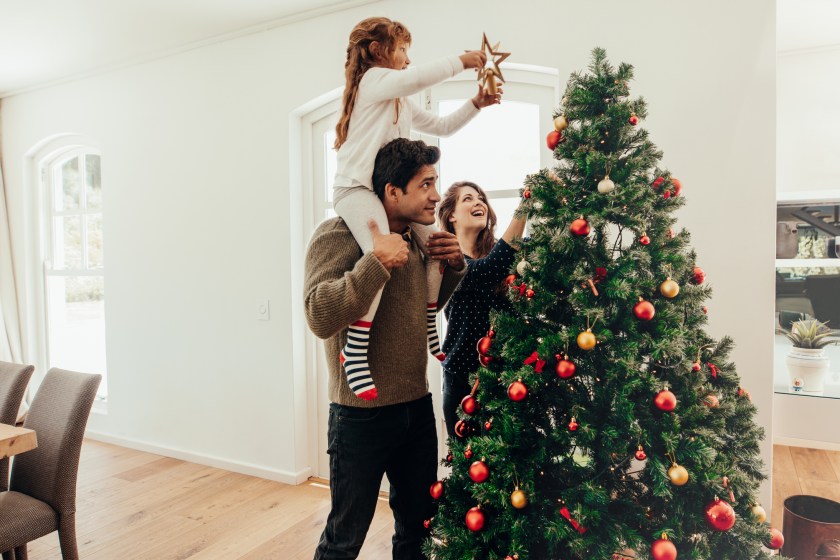 Family decorating a Christmas tree. Young man with his daughter on his shoulders helping her decorate the Christmas tree.