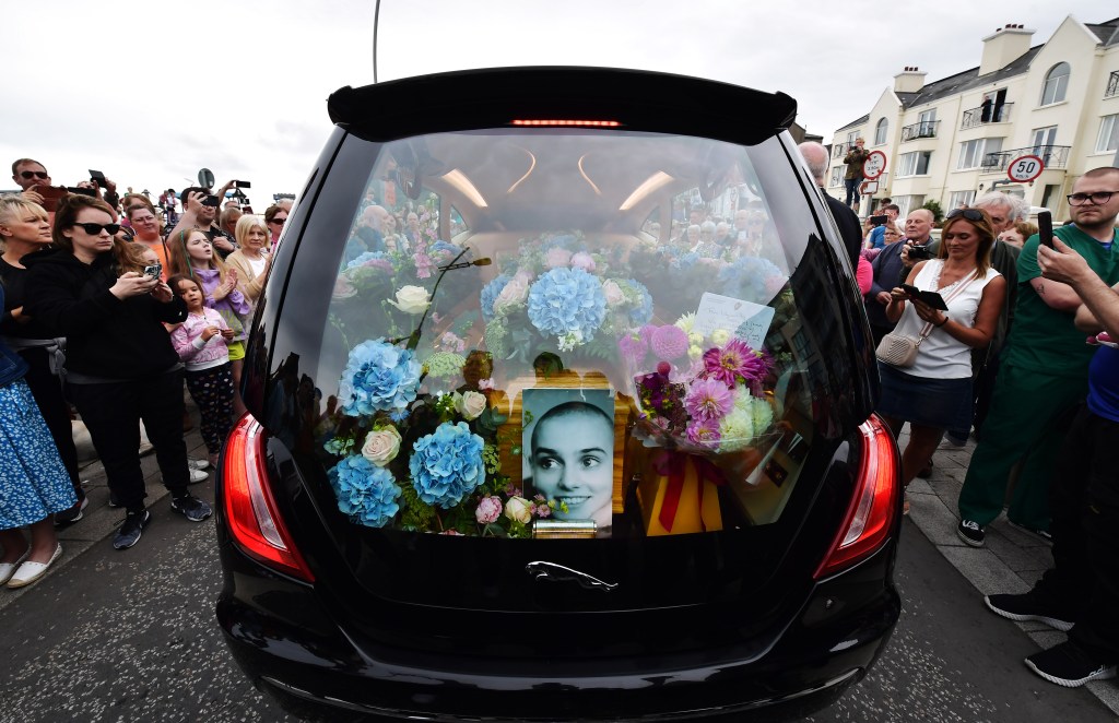 BRAY, IRELAND - AUGUST 8: Crowds of people line the street as the hearse carrying Sinéad O'Connor's coffin passes by her former home on the seafront on August 8, 2023 in Bray, Ireland. The public lined the streets of Bray today as the funeral cortege of Sinéad O'Connor passed through the town where she lived for 15 years. The iconic Irish singer known for her hit single "Nothing Compares 2 U" passed away at the age of 56 on July 26, 2023. O'Connor was renowned as a protest singer who used her fame to champion human rights, anti-racism, and expose injustice, particularly within the Catholic Church. She leaves behind three children.