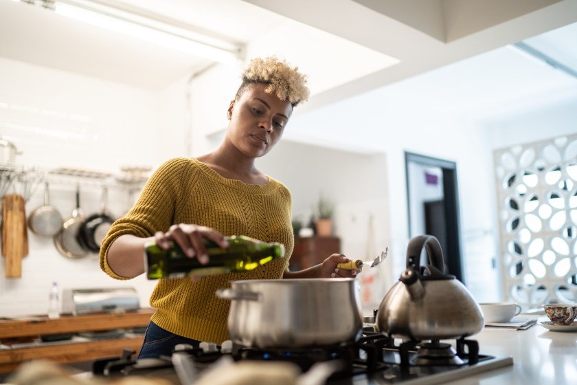 Young woman preparing food at home using olive oil
