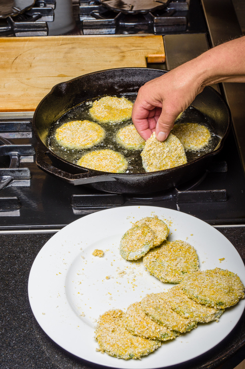 Slices of green tomato being fried to make fried green tomatoes