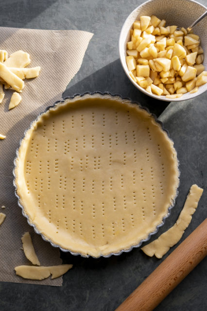Homemade pie crust in pie plate. Cooking apple pie, dark background