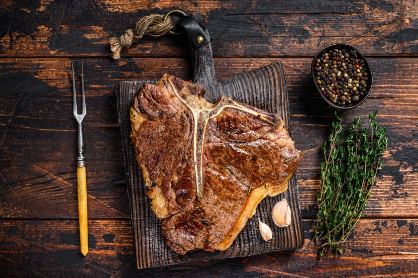 Roast porterhouse beef meat Steak on a wooden cutting board. Dark wooden background. Top view