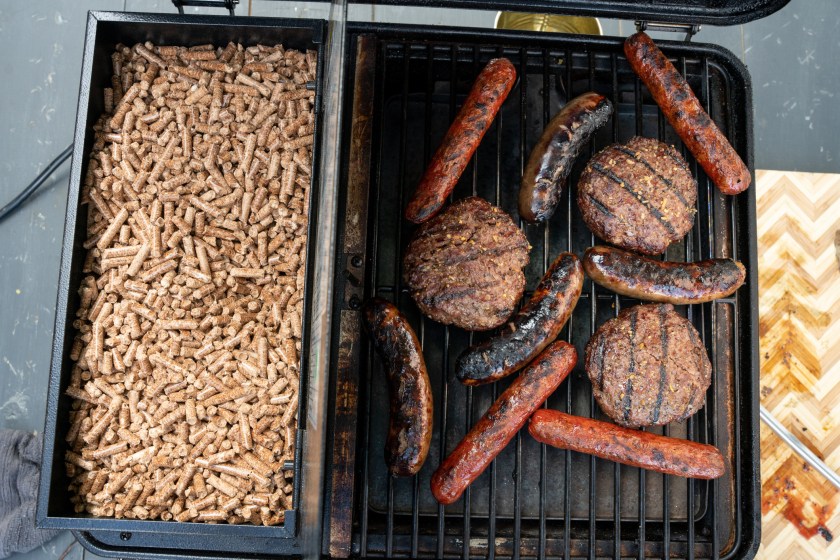 Bratwurst, Grass-Fed Hamburger Patties Cooking In A Portable Smoker, Pellet Hopper Open