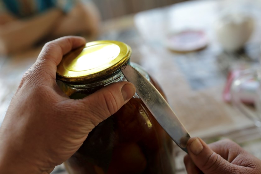 Person opening jar with pickled tomatoes