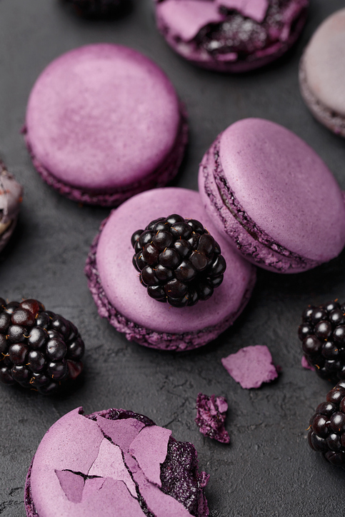 Set of violet and lilac macaroons and blackberries on dark concrete background. Overhead view, close up. Traditional French dessert