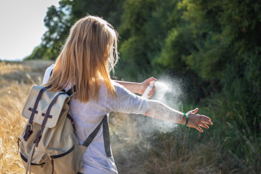 Woman tourist applying mosquito repellent on hand during hike in nature. Insect repellent.