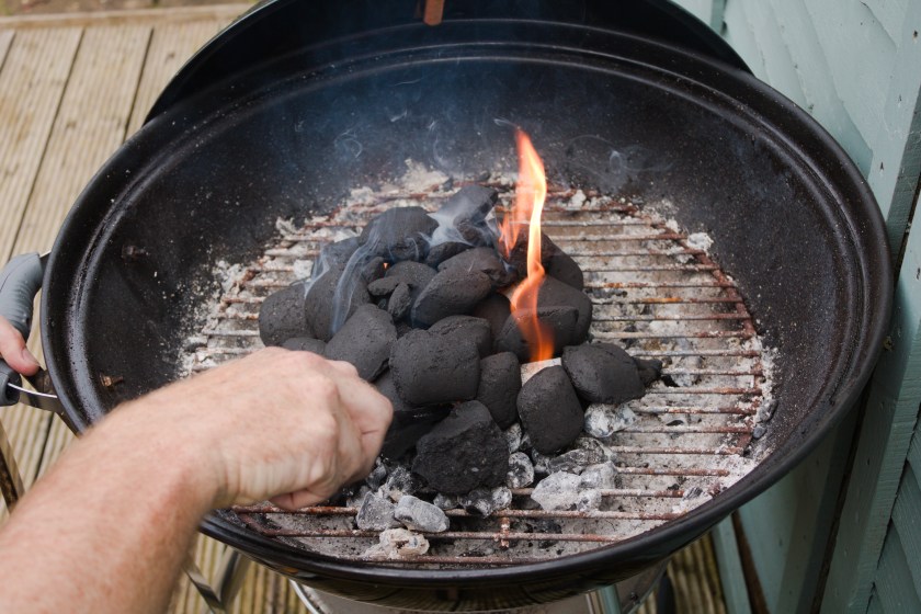 Man's hand holding lighter and lighting coal in bbq grill
