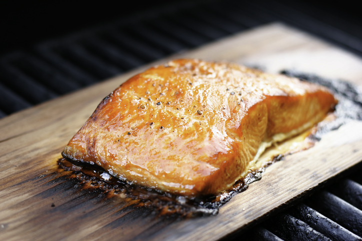 Salmon fillet with coarse ground pepper, grilled over a cedar plank. This cooking method gives the salmon great cedar smoke flavor and color. Shallow dof.