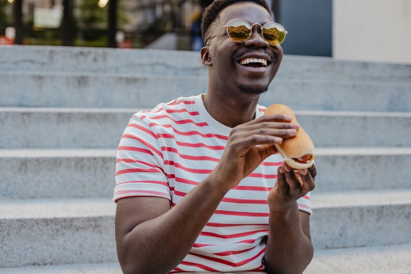 Young African-American man is eating hot dog and smiling