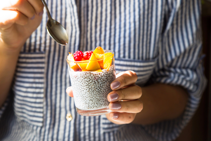 Chia pudding on coconut milk with raspberries and peach in a glass jar in female hands with a spoon.