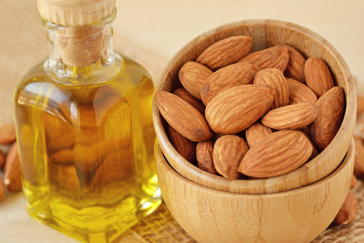 Bottle of almond oil and almonds in wooden bowl