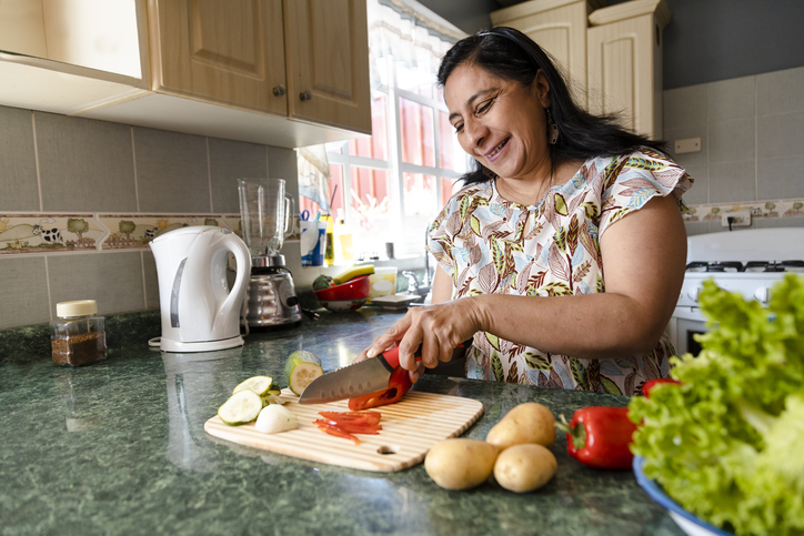 Mature Woman Cutting Fresh Vegetables In Her Kitchen