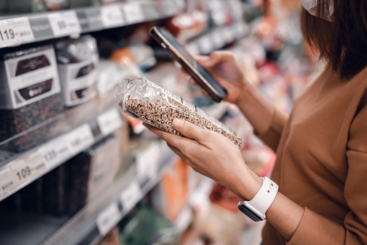 Closeup - Woman shopping in supermarket and reading product information. Costumer buying food at the market.