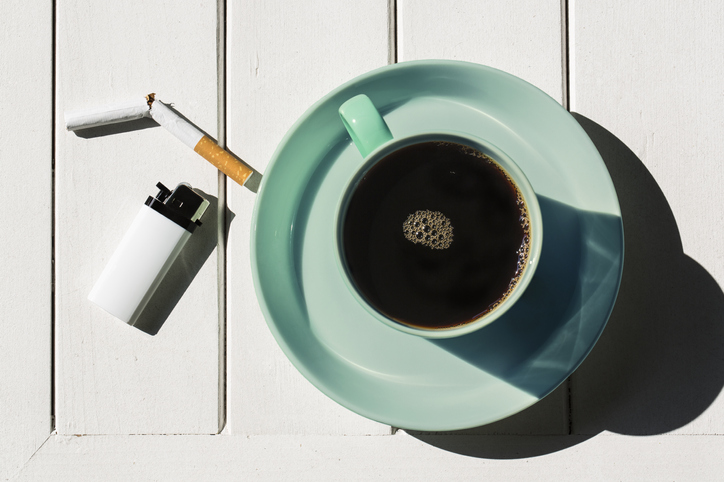 Cup of coffee with cigarettes on the wooden plank table.