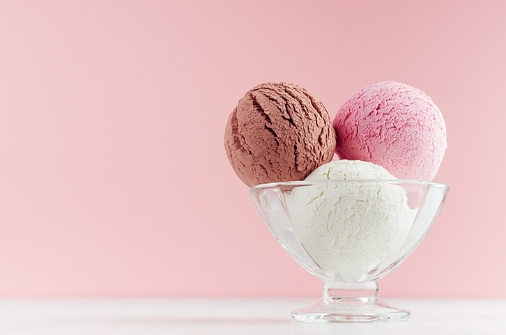 Ice cream scoops different flavor - strawberry, chocolate, creamy in transparent glass ice-cream bowl in modern pink color interior on white wood board.