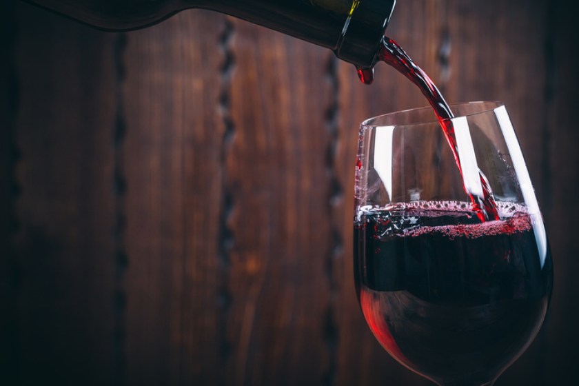 Pouring red wine into the glass against wooden background