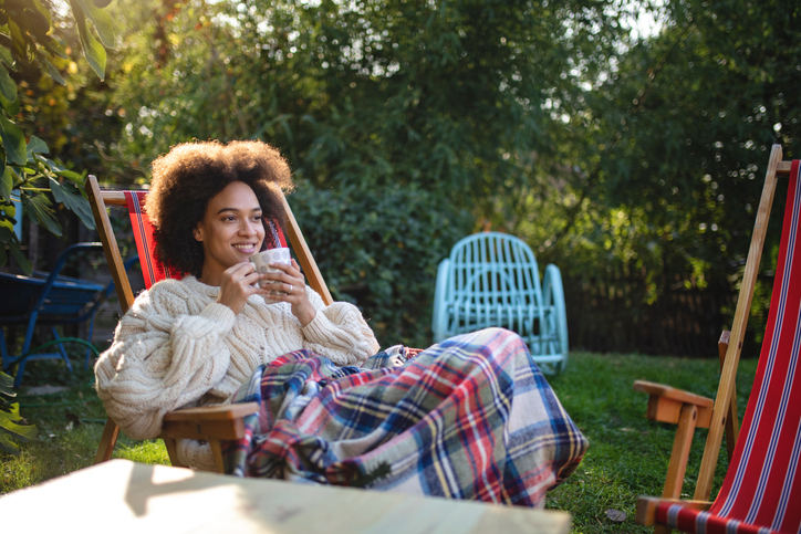 Lovely and serene mixed ethnicity woman enjoying a spring day outdoors in a back yard, sitting on a lounge chair and drinking tea.