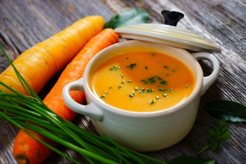 Carrot soup in a white bowl with lid and carrots on the side