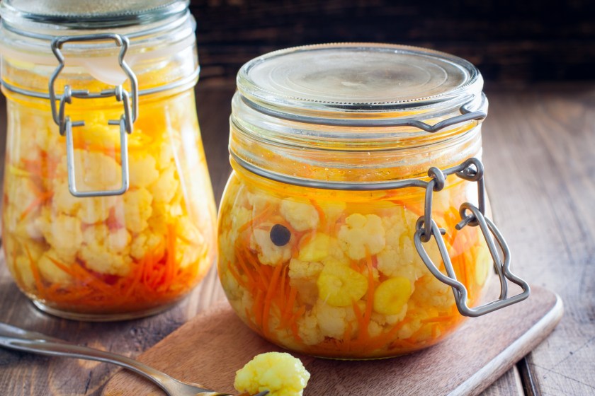 Pickled cauliflower with carrots in glass jars on a wooden table, horizontal