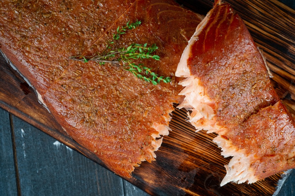 A half-torn piece of smoked salmon fillet on a wooden Board on a dark background