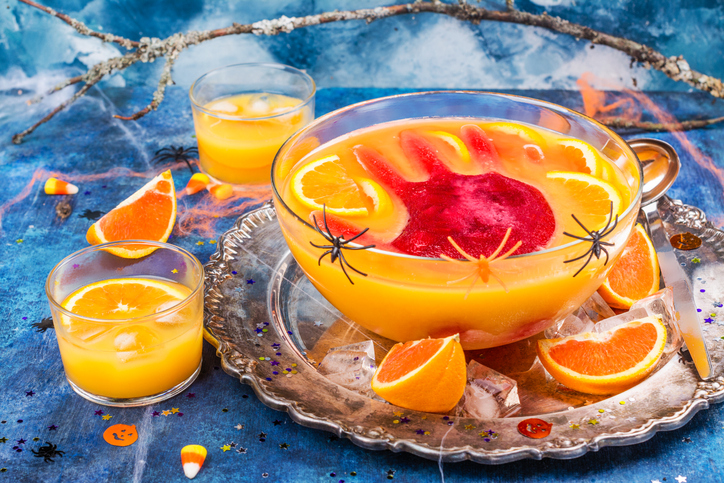 Ghoul's orange punch with bloody ice hand in a glass bowl on dark halloween background