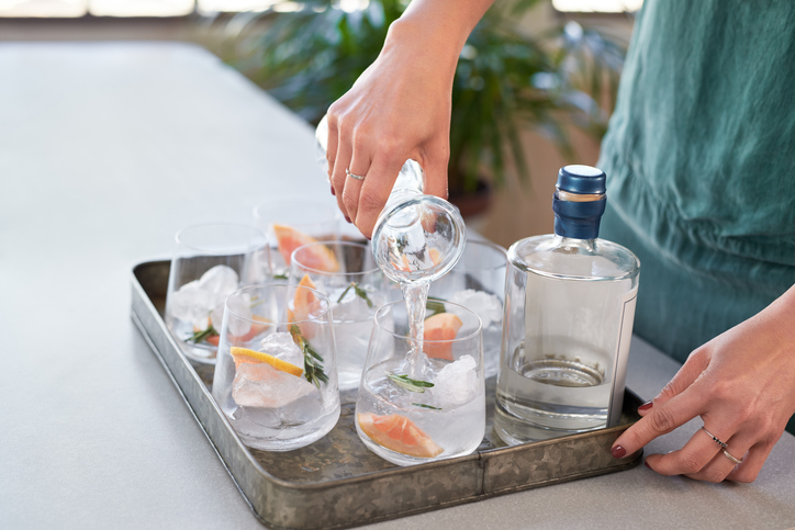 Woman pouring tonic soda water into glasses, preparing alcoholic beverages at a party
