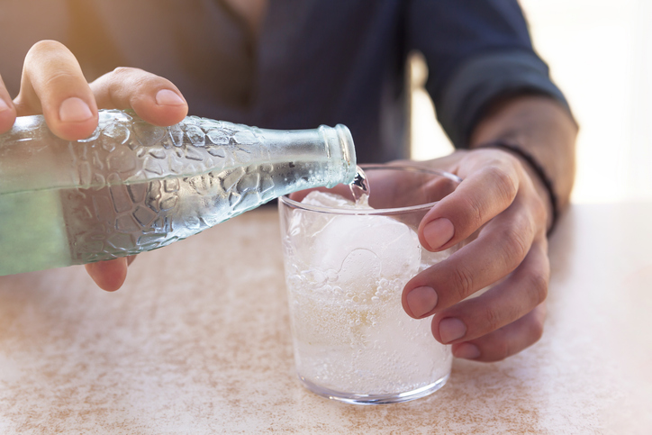 close-up adult man's hand pouring sparkling water into a glass of water outdoors